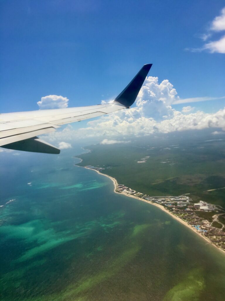 View from the airplane window of the turquoise Caribbean coastline and reef during descent toward Tulum