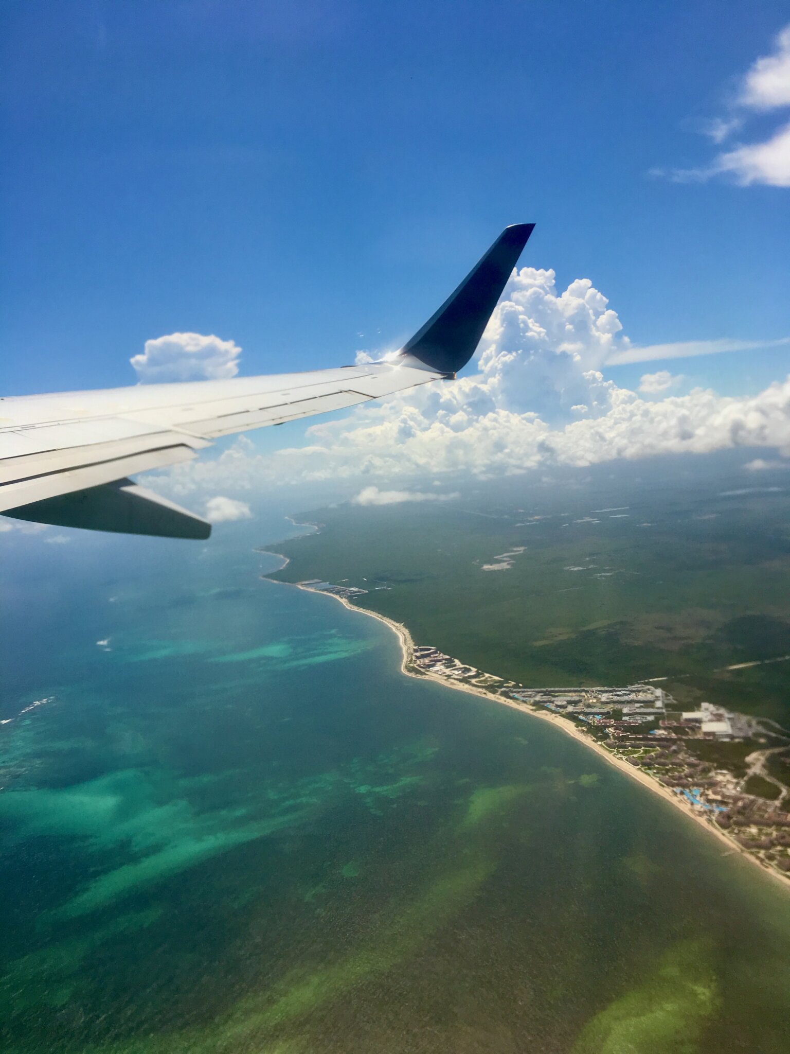 View from the airplane window of the turquoise Caribbean coastline and reef during descent toward Tulum