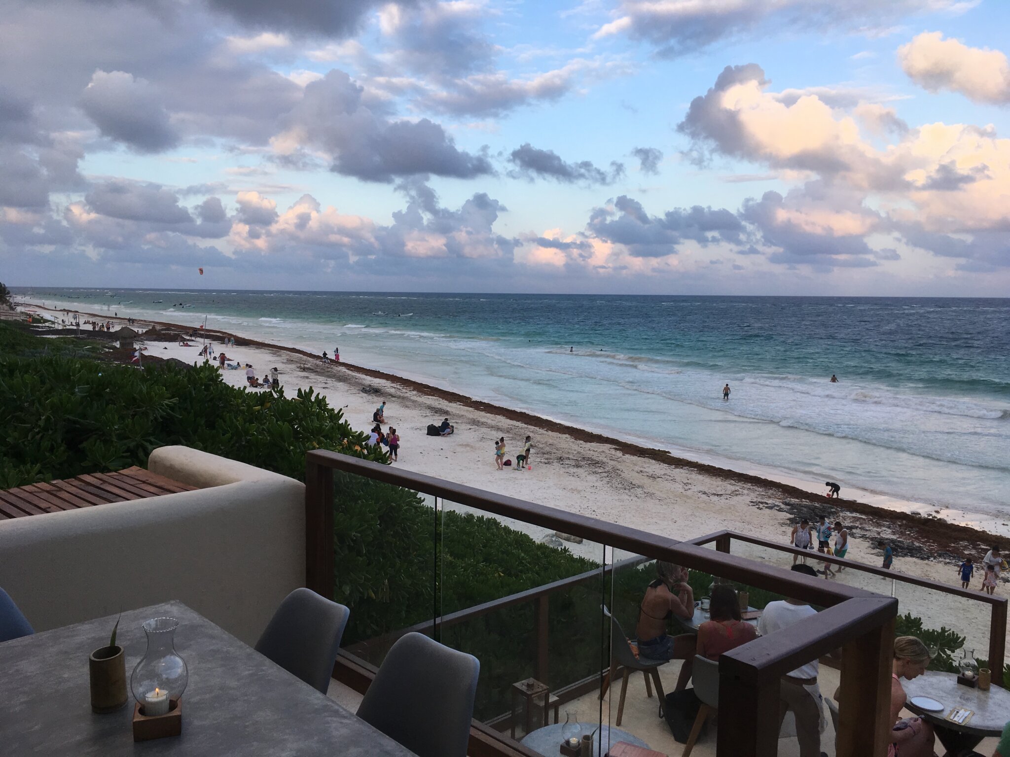 View of a Tulum beach at dusk from a beachside restaurant terrace, with visitors on the sand and in the water