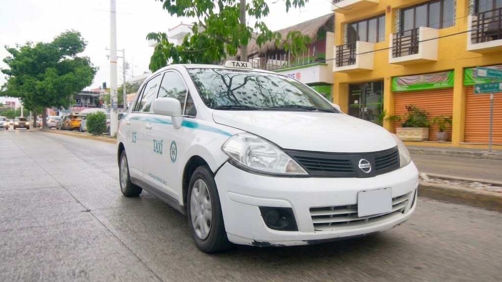 A white Tulum taxi with roof sign parked on a town street